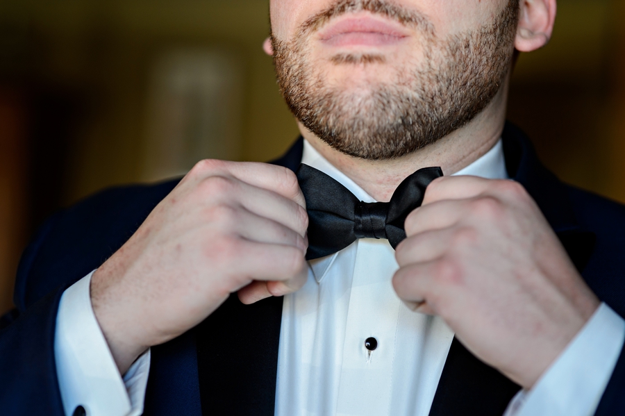 A groom tying his bow tie in the mirror.